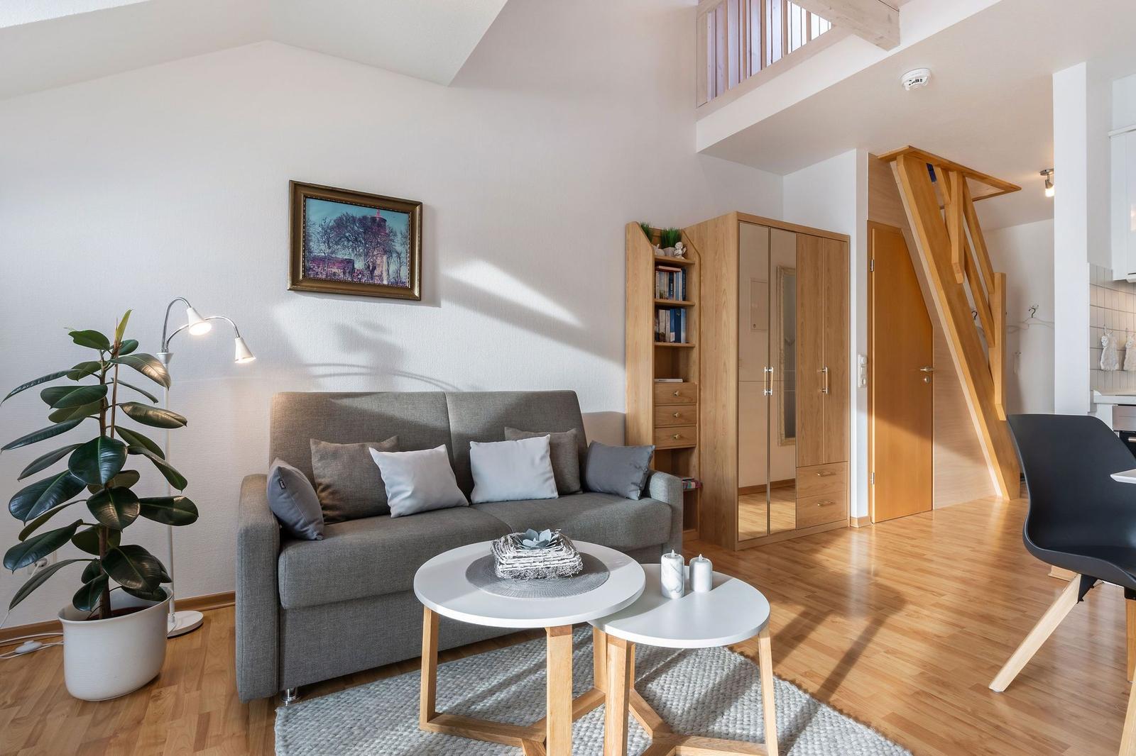Wohnzimmer mit Sofa, Tisch und Pflanze. Holztreppe und Kleiderschrank sichtbar.