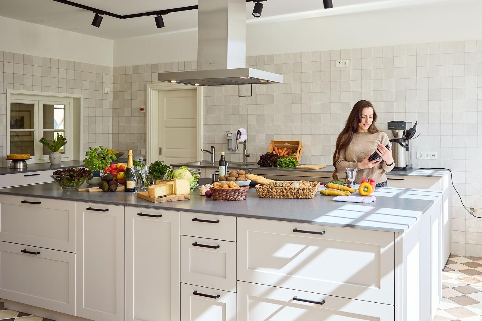 Küche mit Arbeitsplatte, Obst, Gemüse und Frau mit Smartphone.
