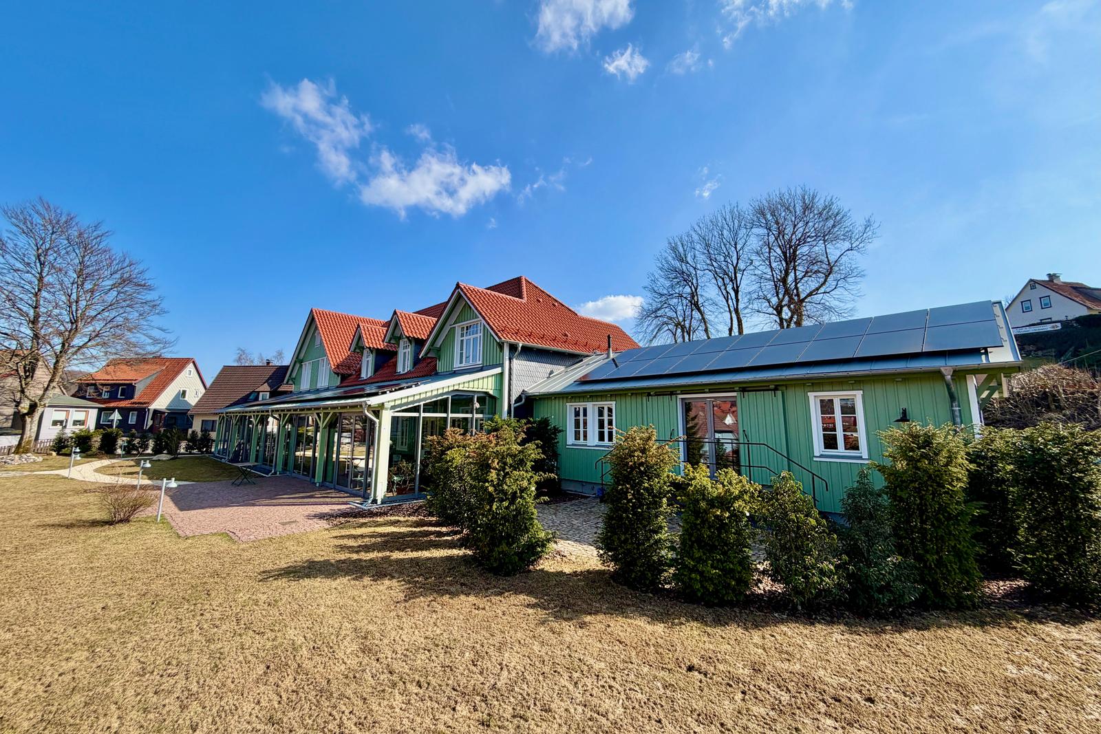 Grünes Haus mit Solaranlage und Terrasse im Freien.