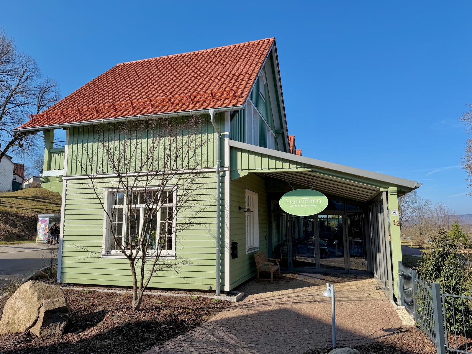 Grünes Haus mit rotem Dach und Eingangsbereich unter Vordach.