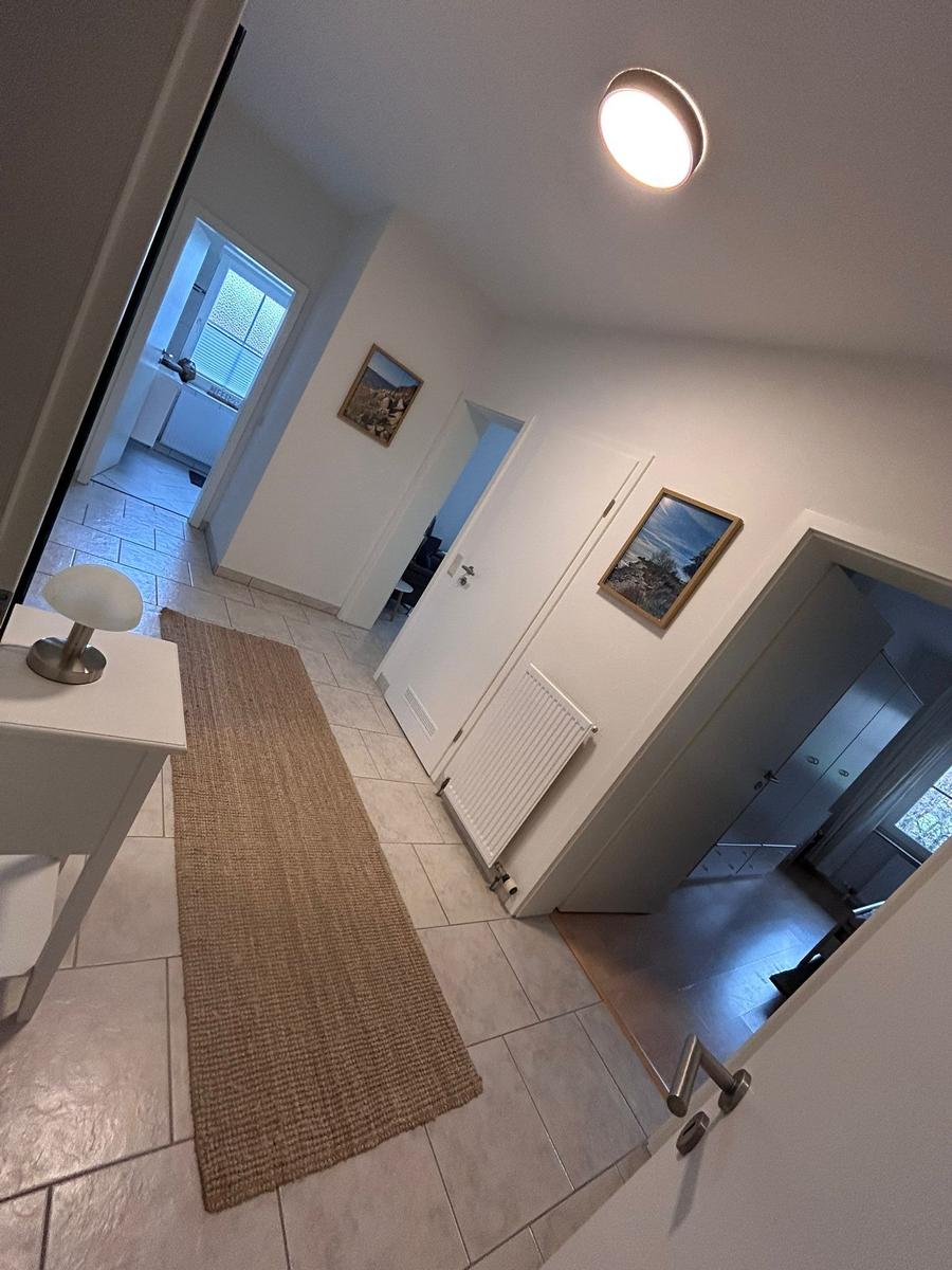 Flur mit Teppich, Tisch und Lampen. Türen führen zu Schlaf- und Badzimmer.