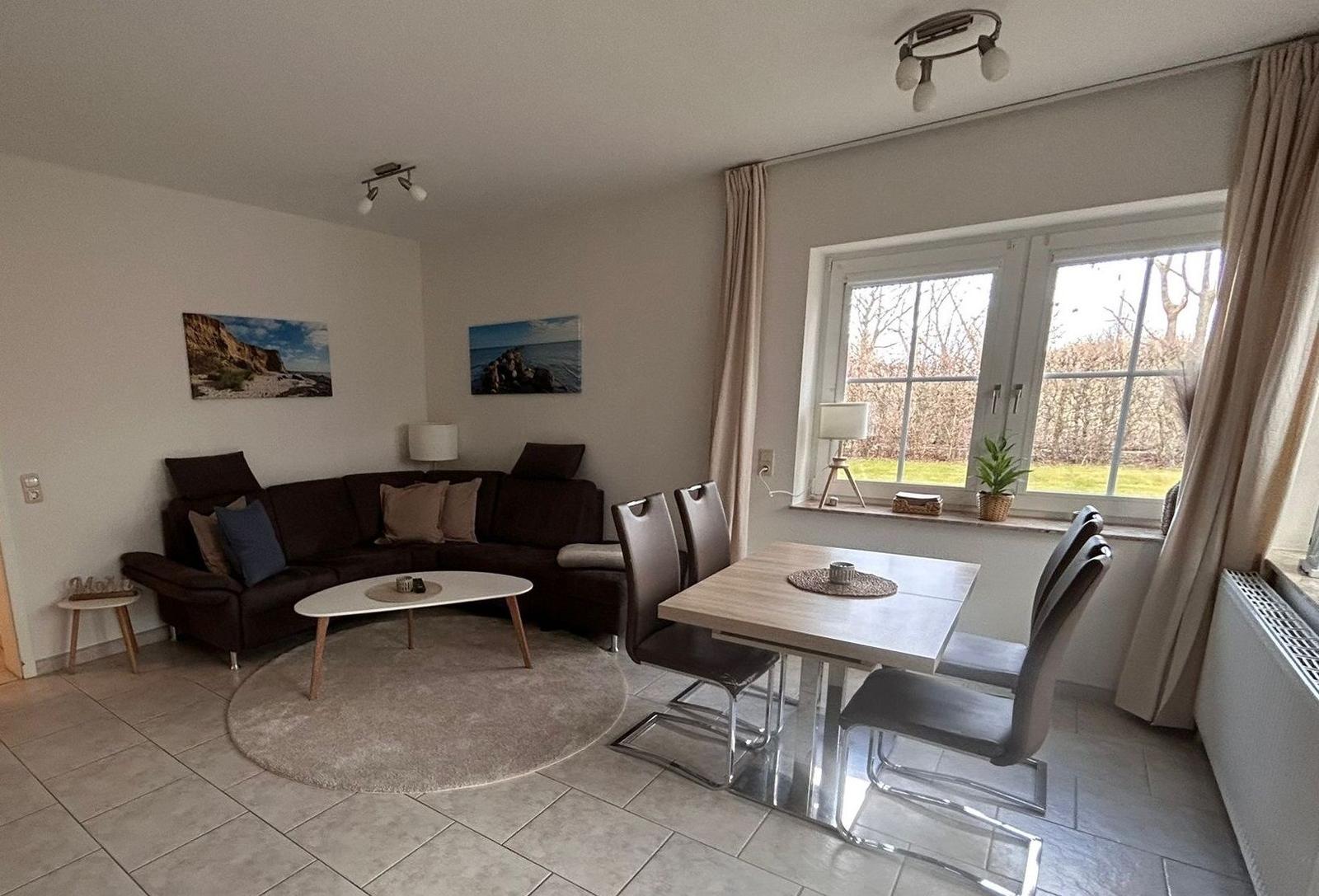 Wohn- und Essbereich mit Sofa, Tisch und Stühlen. Fenster mit Blick auf Garten.