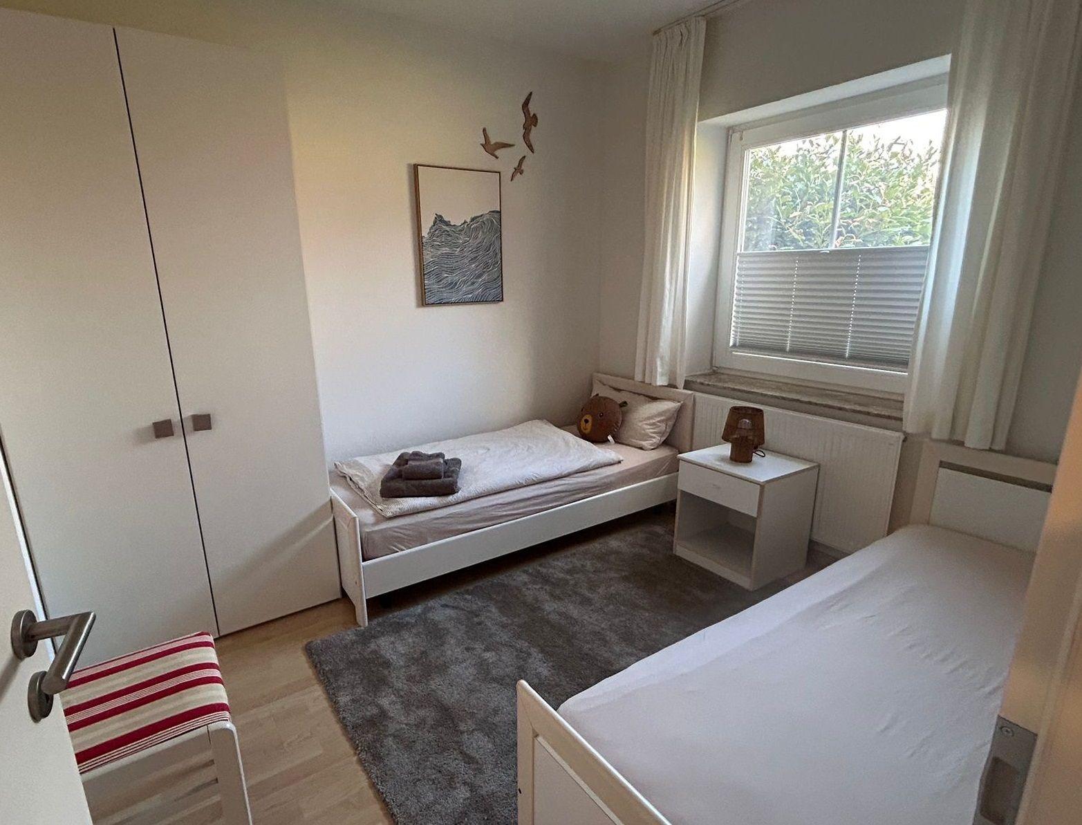 Zimmer mit zwei Betten, Kleiderschrank und Fenster mit Blick auf Grün.