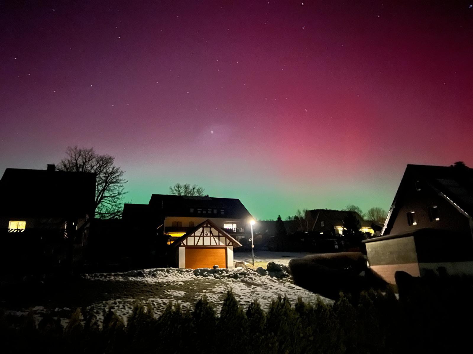 Nachtansicht mit Sternenhimmel und schneebedecktem Grundstück vor Häusern.