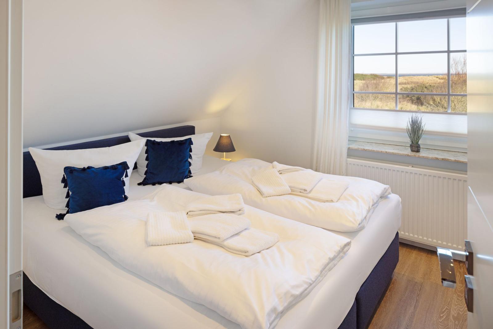 Schlafzimmer mit Doppelbett, Fensterblick und gefalteten Handtüchern.
