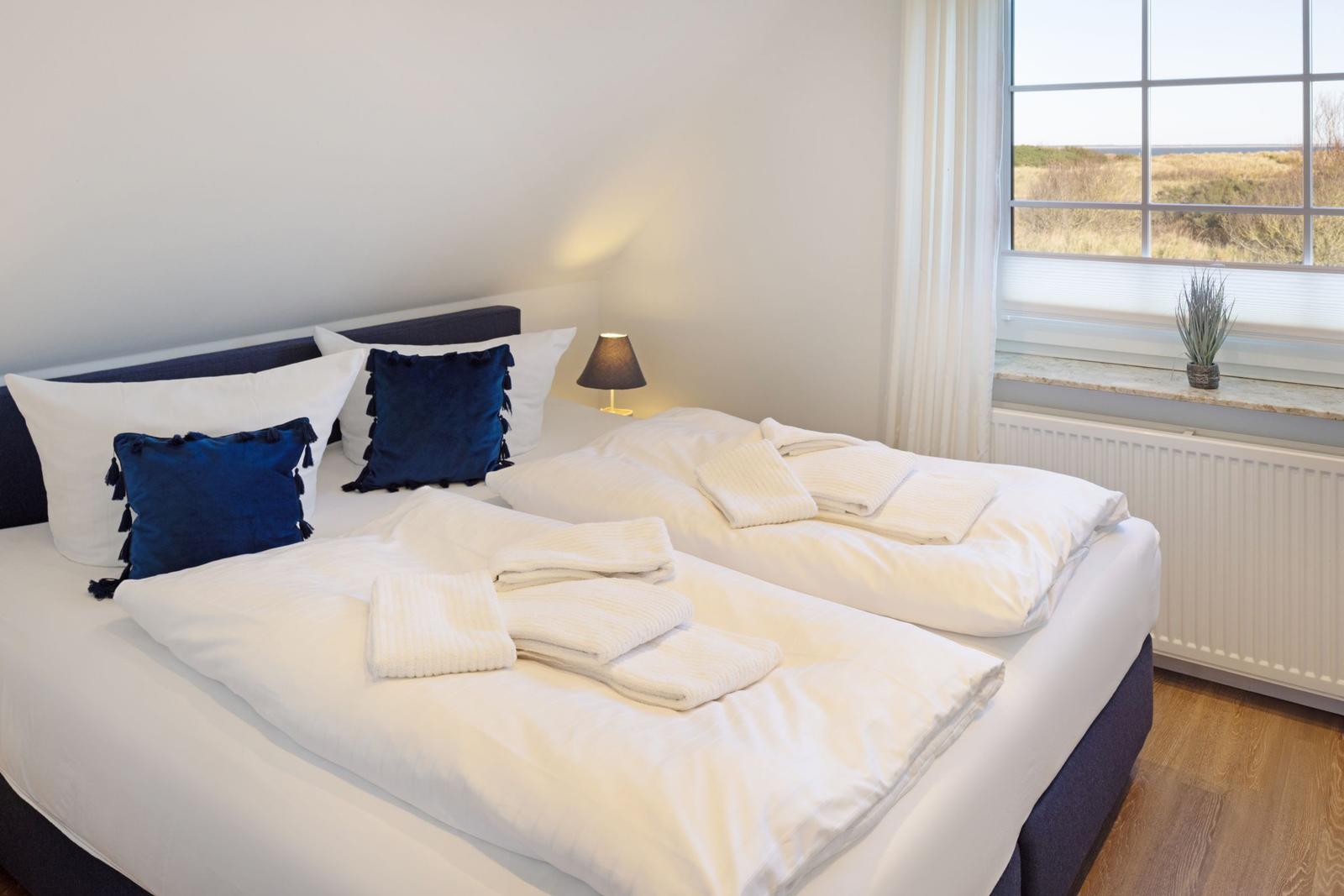 Schlafzimmer mit Doppelbett, Fensterblick und gefalteten Handtüchern.