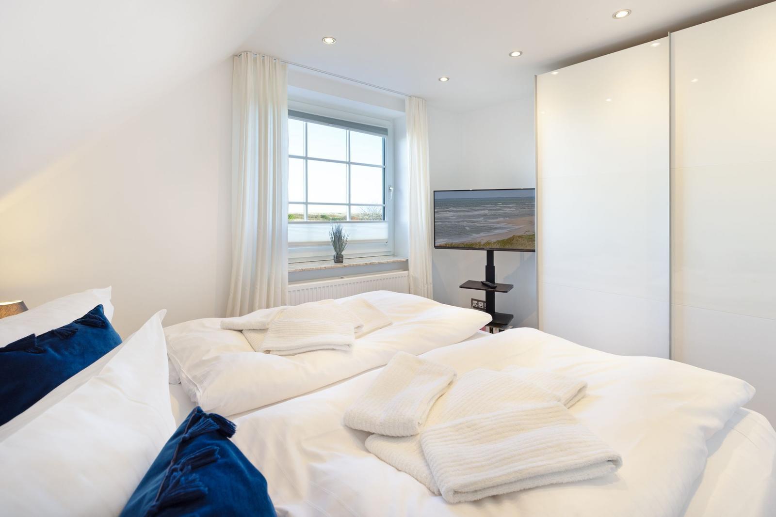 Schlafzimmer mit Bett, TV und Fenster mit Blick auf Strand.