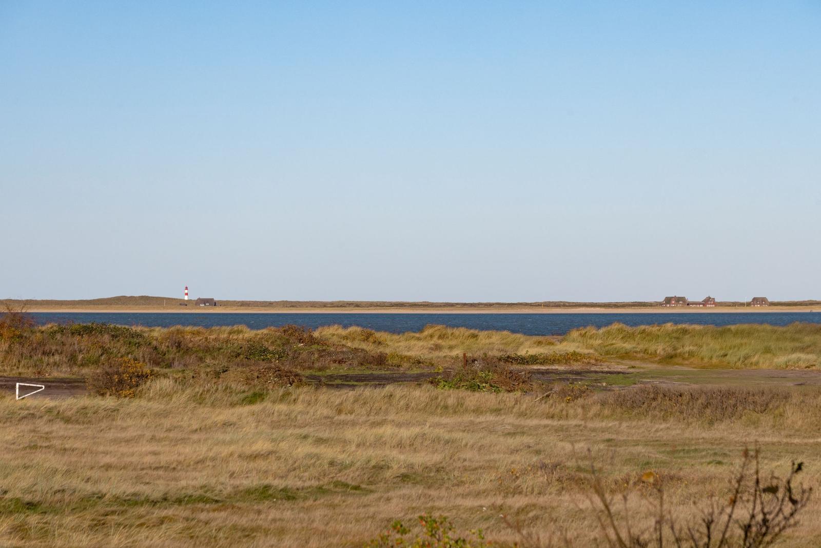 Weitläufiger Blick auf Strand mit Leuchtturm und Dünen im Hintergrund.