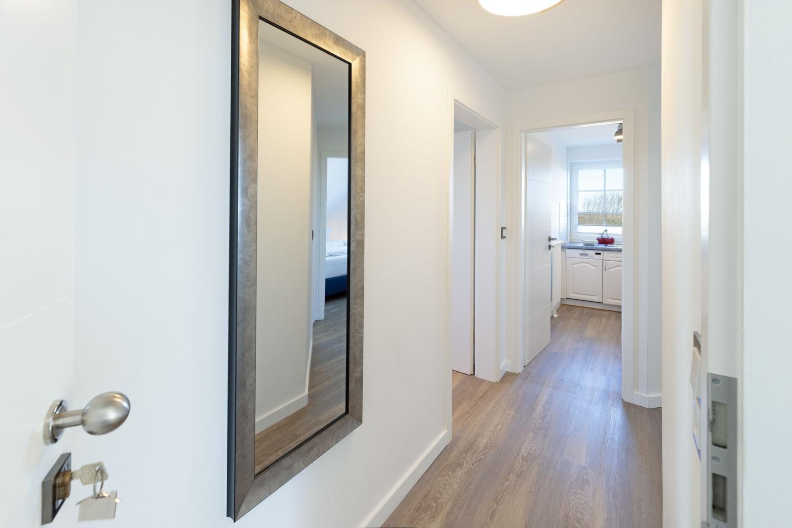 Flur mit Spiegel, Holzboden und Blick in Küche und Schlafzimmer.