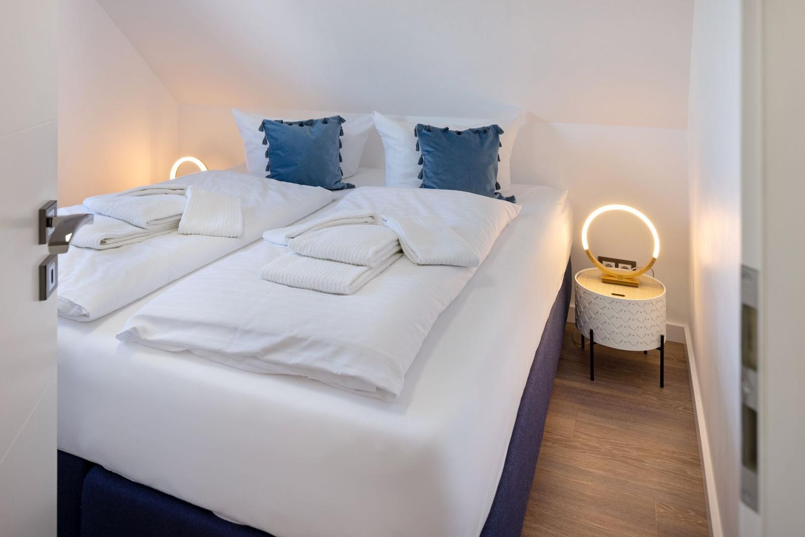 Schlafzimmer mit Doppelbett, blauen Kissen und runden Nachttischen mit Beleuchtung.