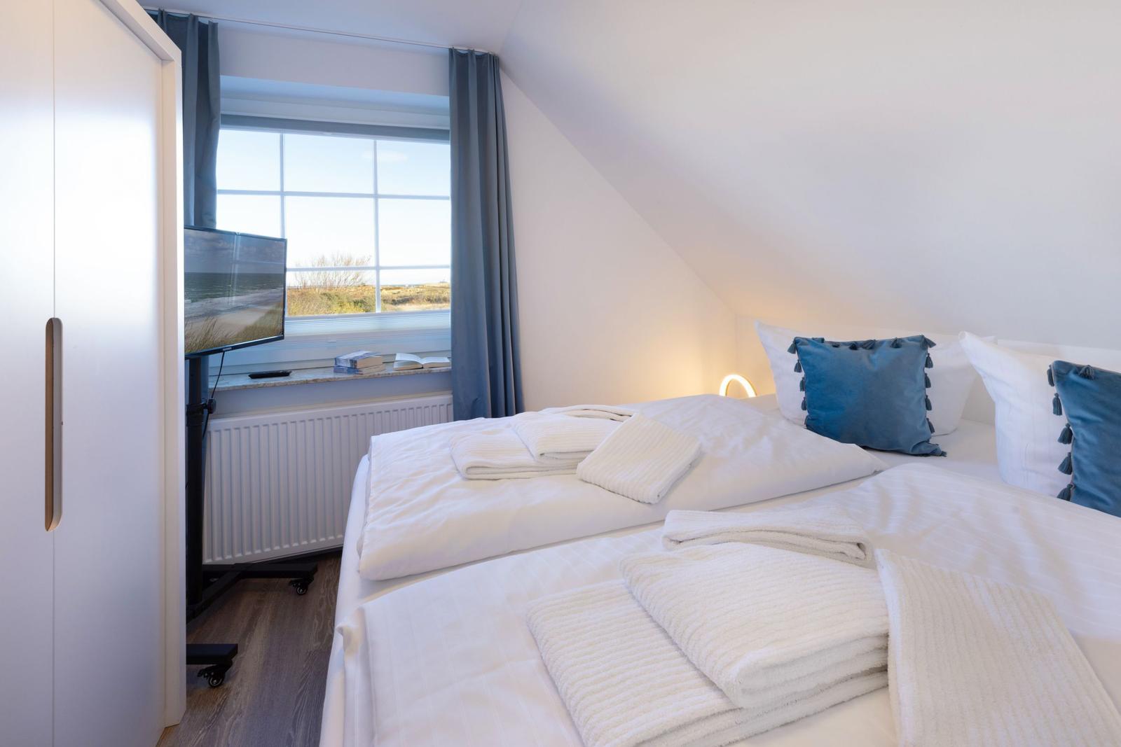 Schlafzimmer mit Doppelbett, Fenster und TV.