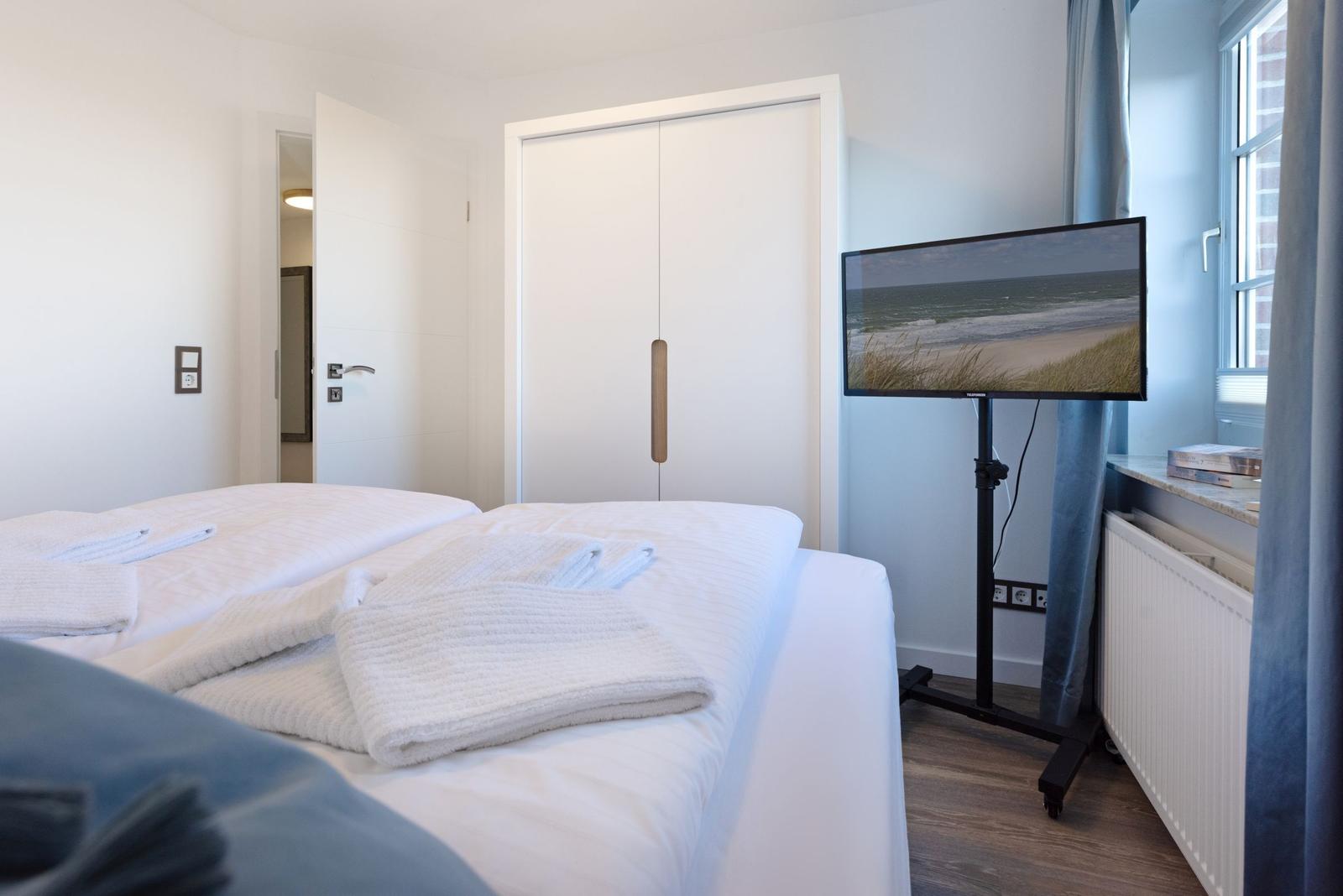 Schlafzimmer mit Bett, TV und Garderobe.