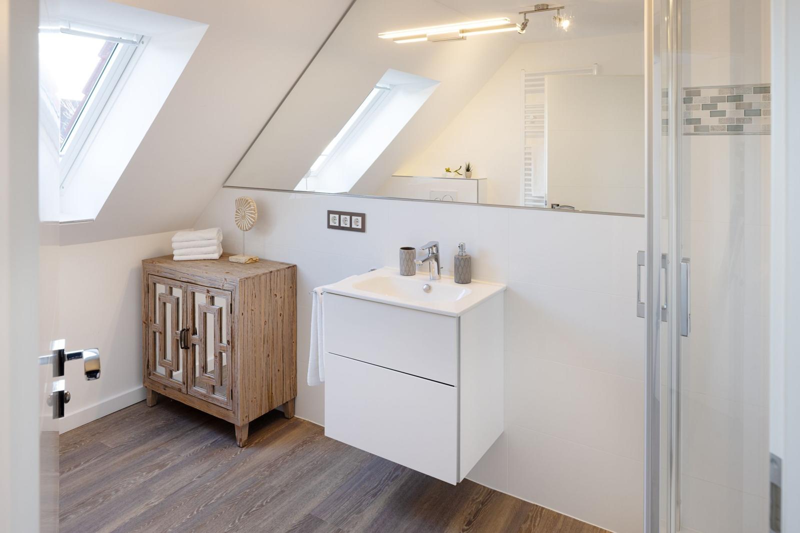 Badezimmer mit Dachschrägen, Waschbecken, Dusche und Holzschrank.