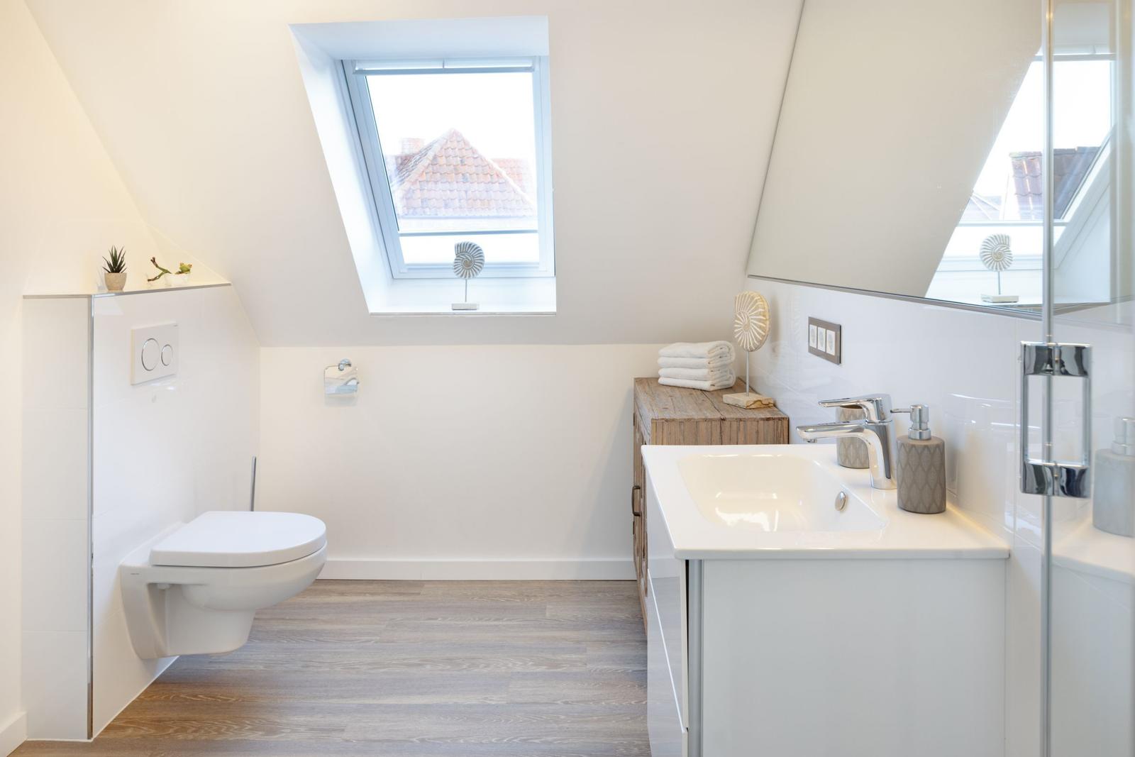 Dusche, Waschbecken und Toilette unter Dachschrägen mit Fenster.