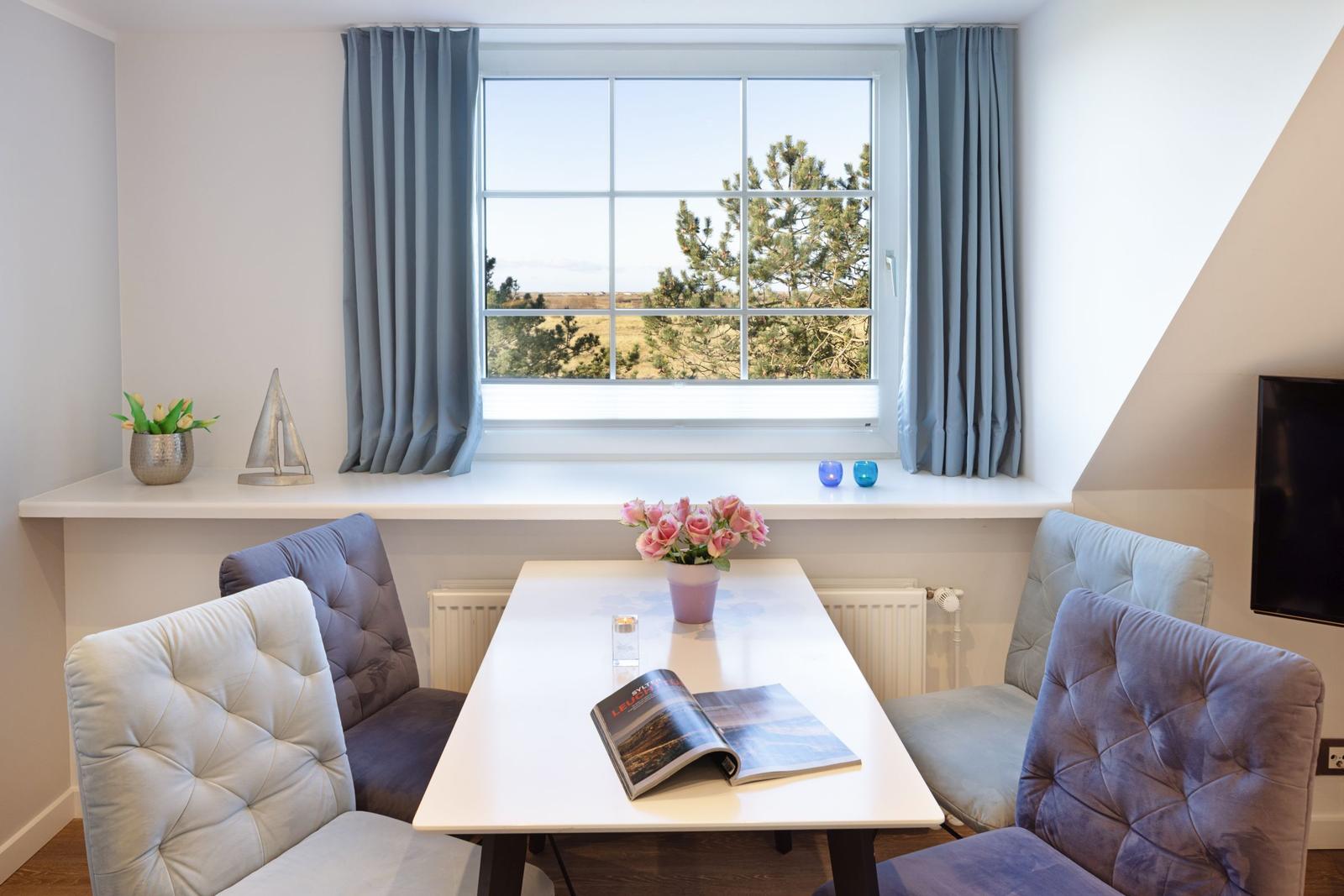 Essbereich mit Tisch, Stühlen und Fensterblick auf Landschaft.