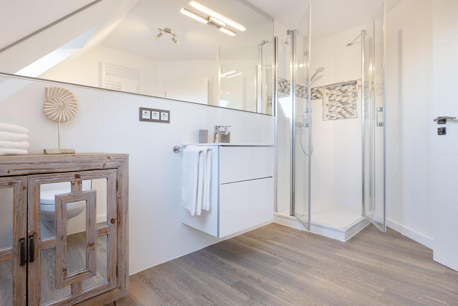 Badezimmer mit Dusche, Waschbecken und Holzschrank.