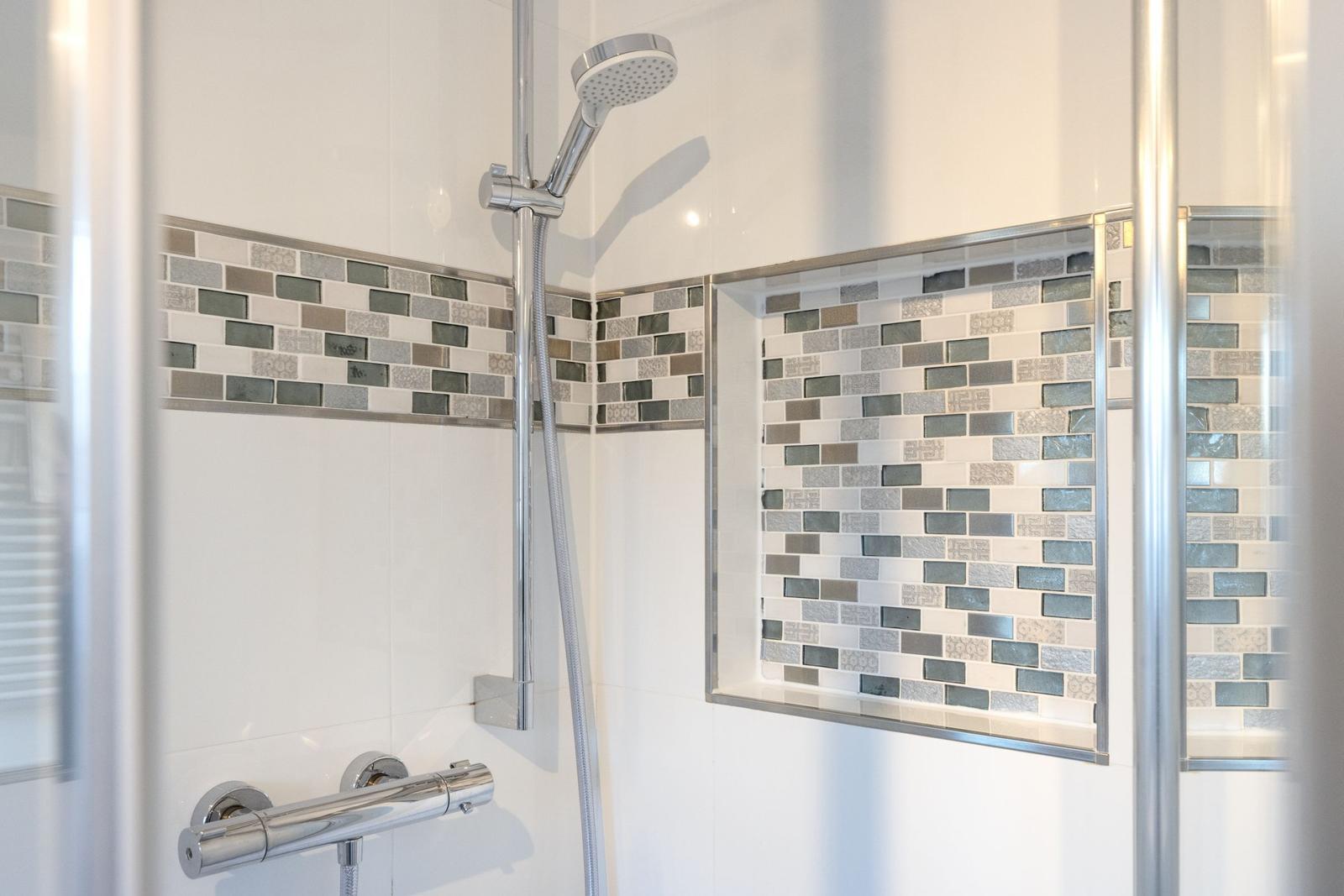 Duschkabine mit Glaswand, Mosaikfliesen und Duschbrause