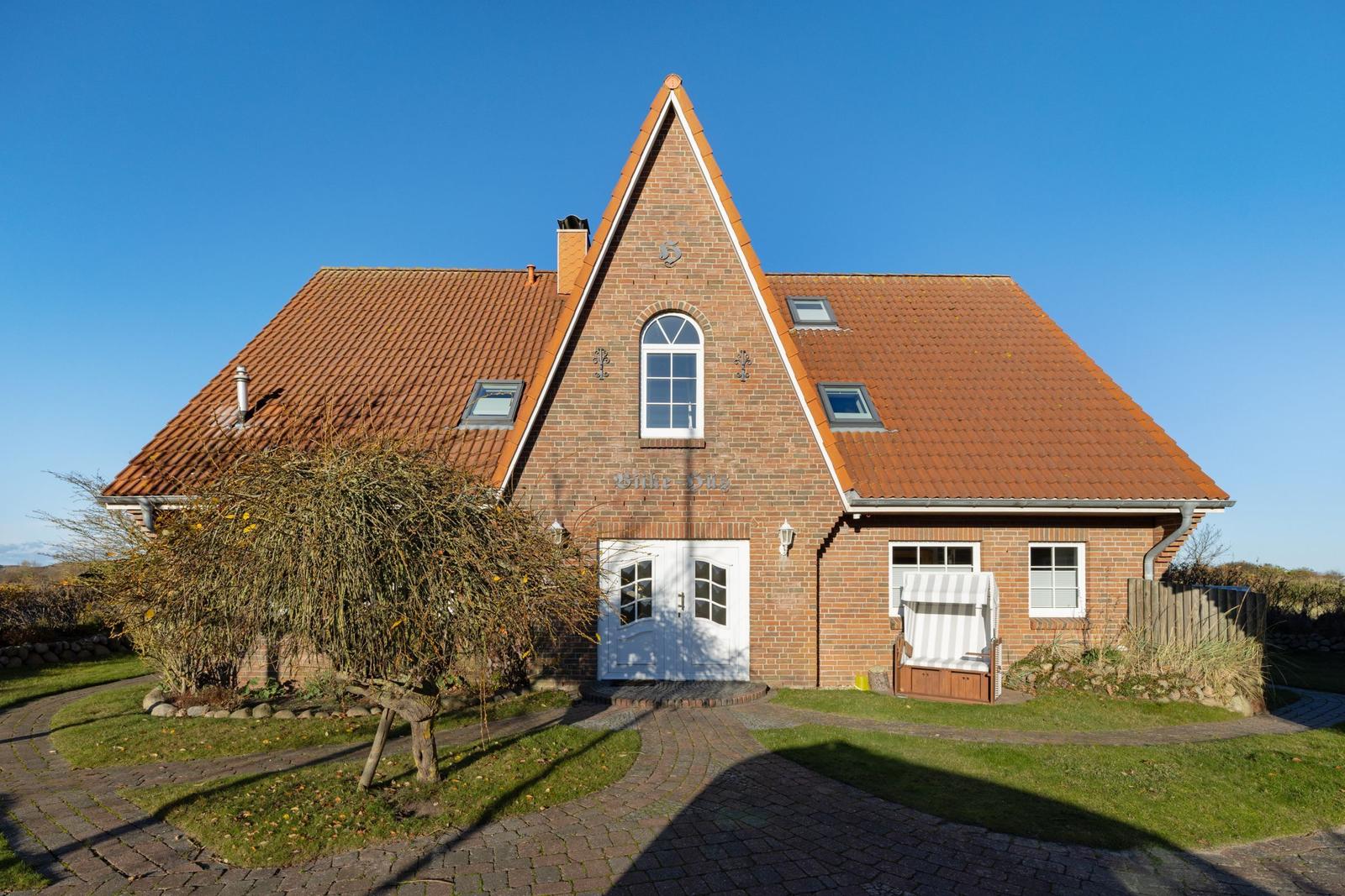Rotes Ziegeldach, weiße Tür, Gartenweg und Bäume vor einem Haus.