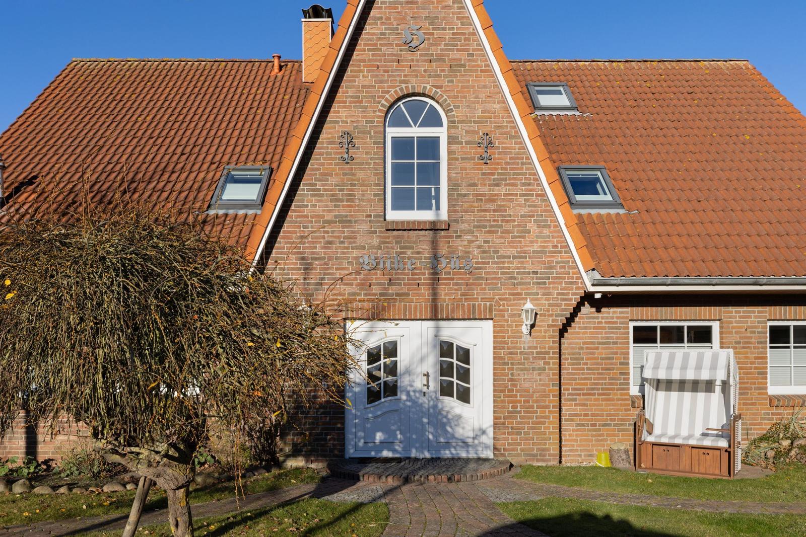 Haus mit rotem Ziegeldach, weißer Eingangstür und Gartenliege.