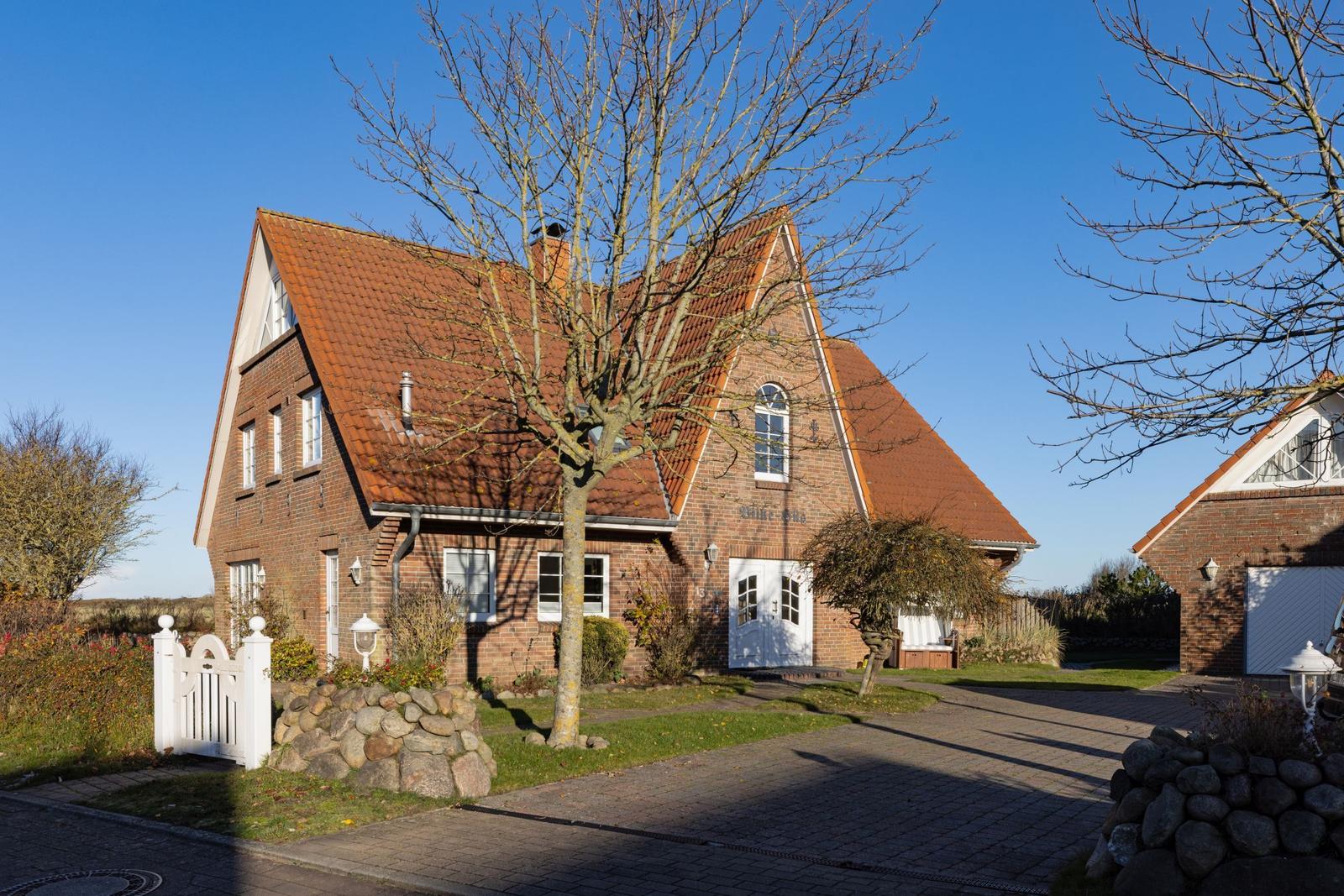 Ein zweistöckiges Haus mit rotem Dach und weißer Tür. Vor dem Haus steht ein Baum.