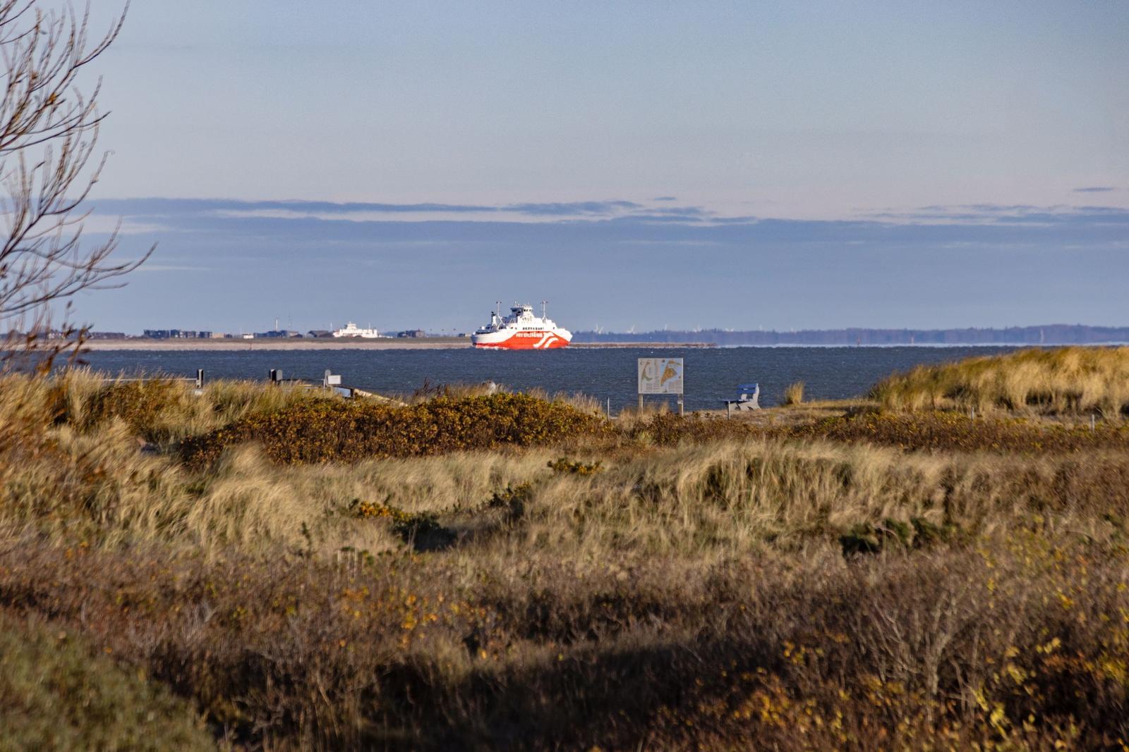 Rotes Schiff auf dem Wasser, umgeben von Dünen und Vegetation.