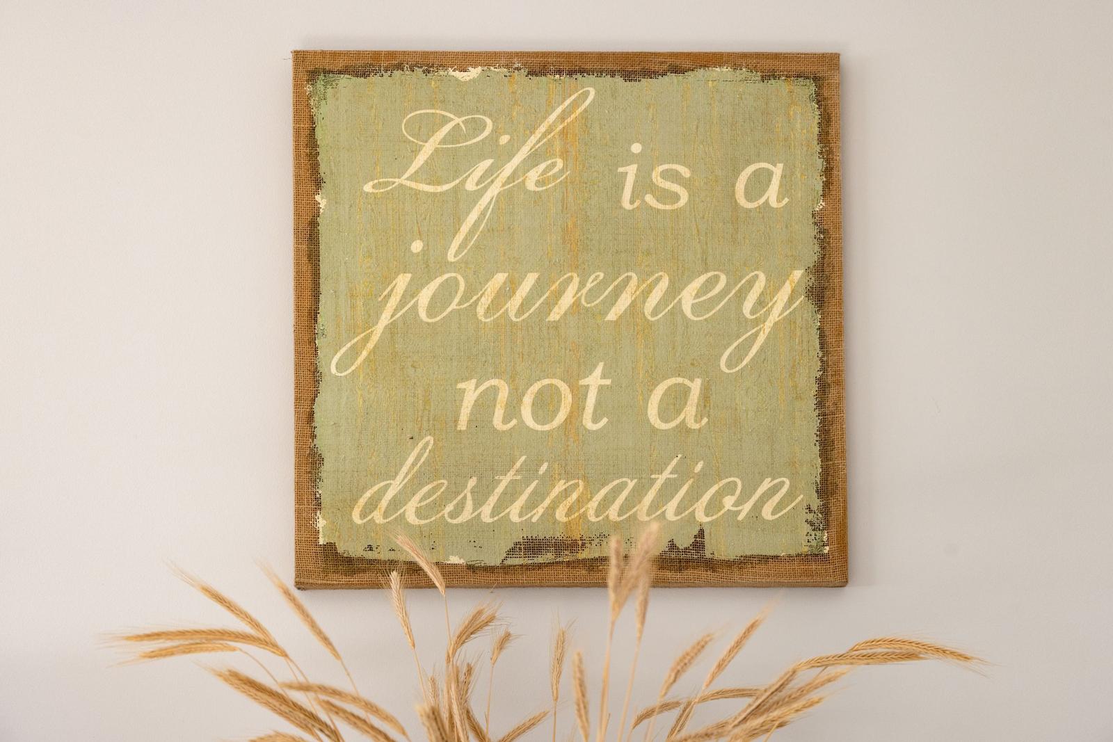 Wandbild mit der Aufschrift Leben ist eine Reise nicht eine Destination, unterlegt mit getrockneten Ähren.