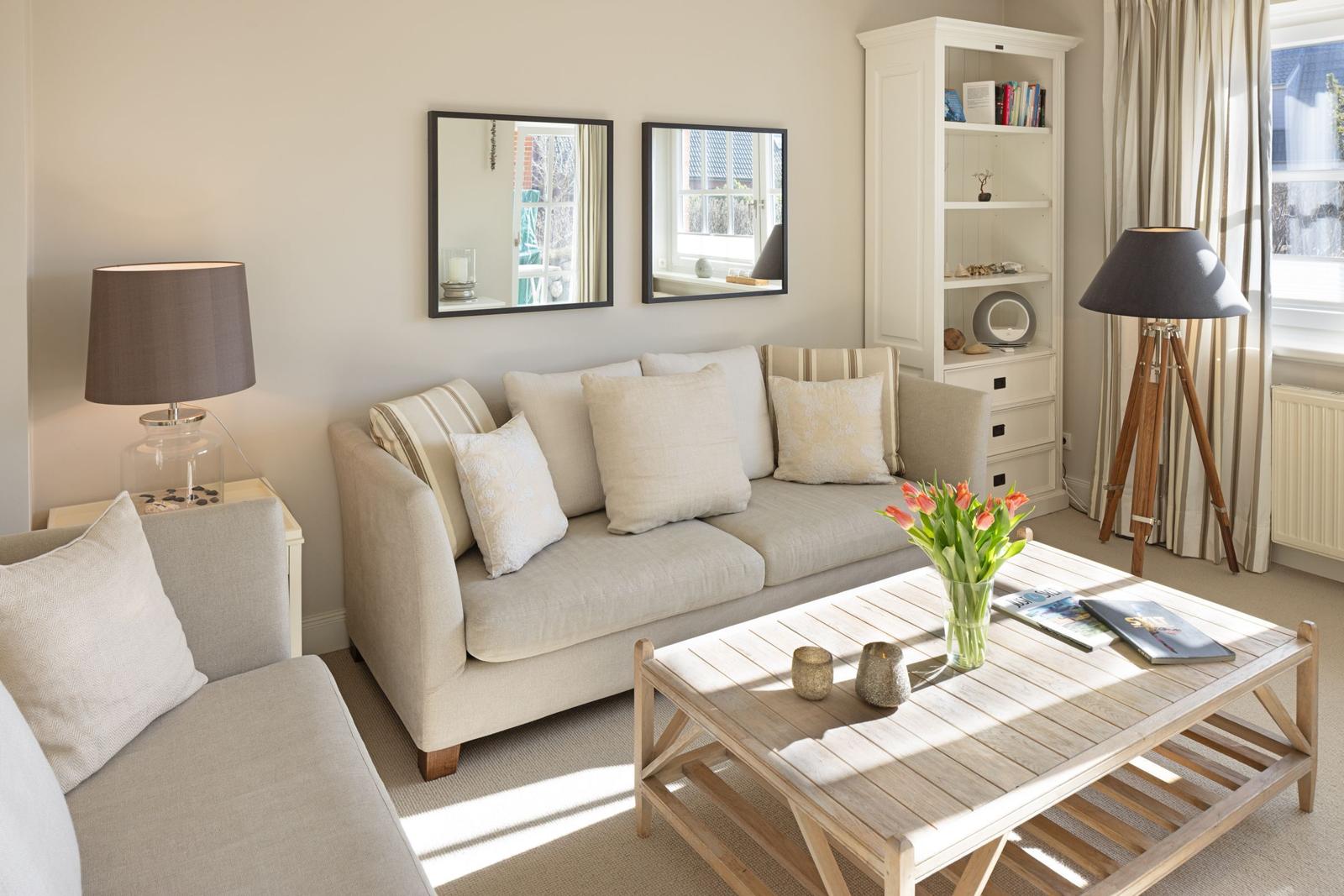 Wohnzimmer mit Sofa, Couchtisch und Bücherregal. Fenster mit Vorhängen und Stehlampe.