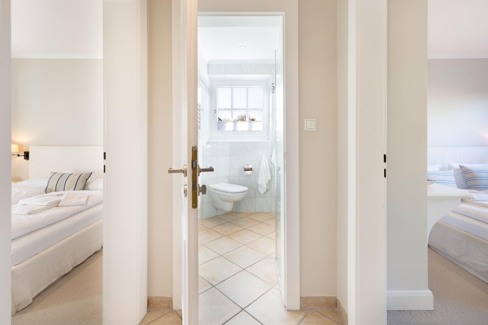 Badezimmer mit Toilette und Fenster. Zwei Schlafzimmer sind sichtbar.