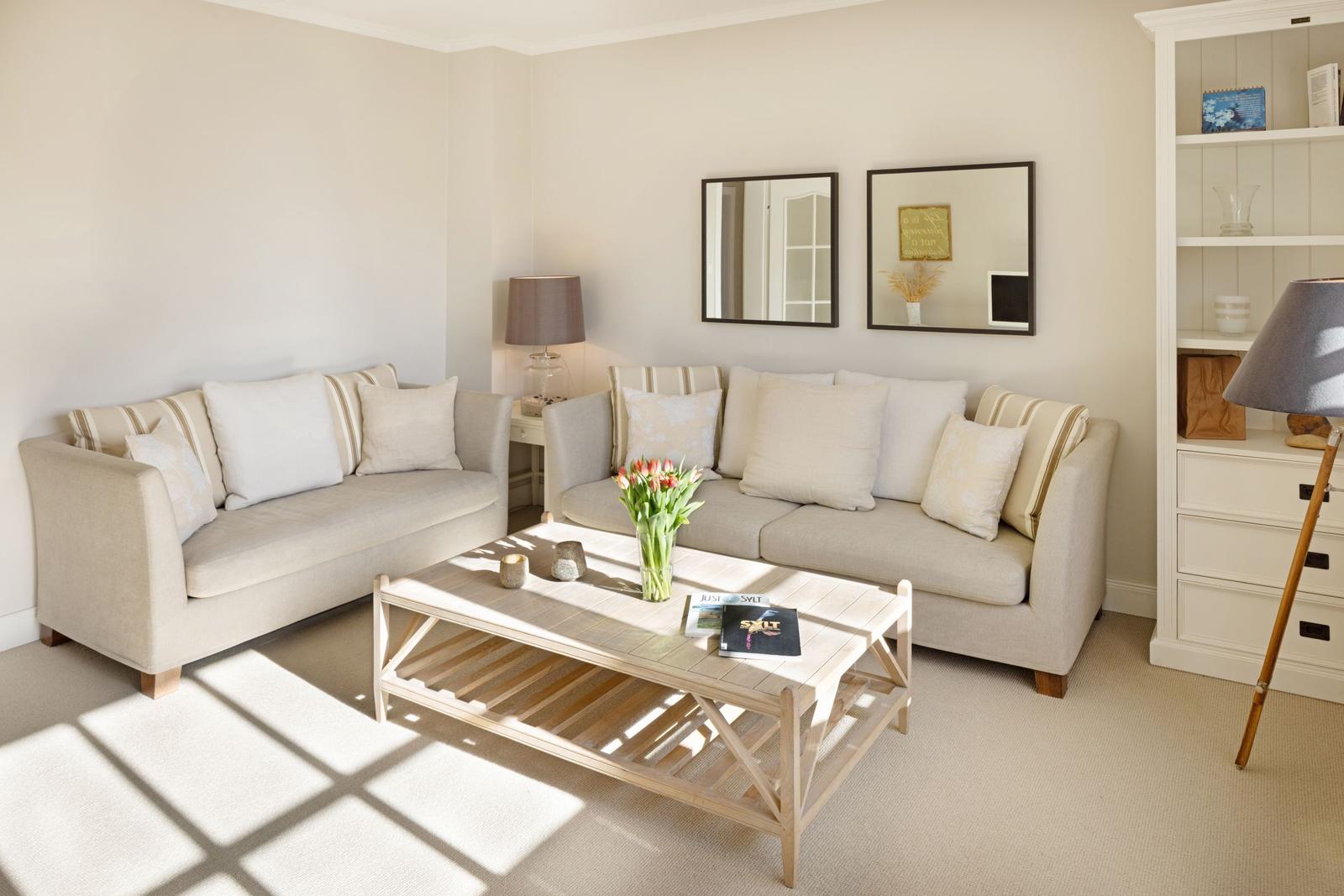 Zwei Sofas mit Kissen, Couchtisch mit Blumen und Wandspiegel.