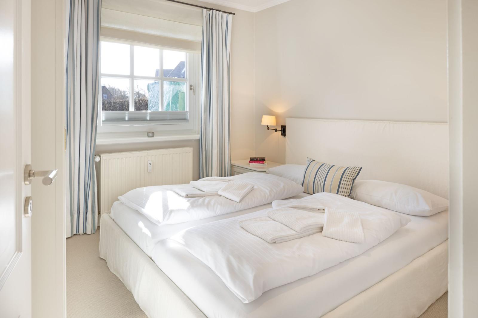 Schlafzimmer mit Doppelbett, Fenster und Vorhängen.
