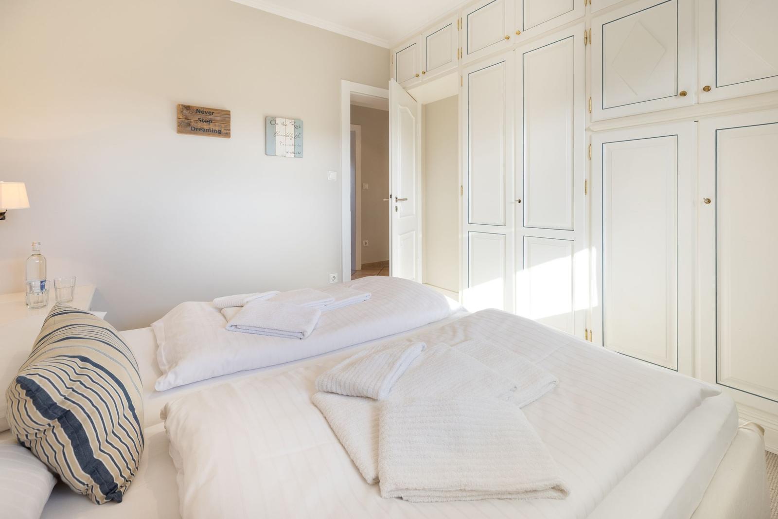 Schlafzimmer mit Bett, Kissen und Schränken. Wanddekoration und Wasserflasche auf Nachttisch.
