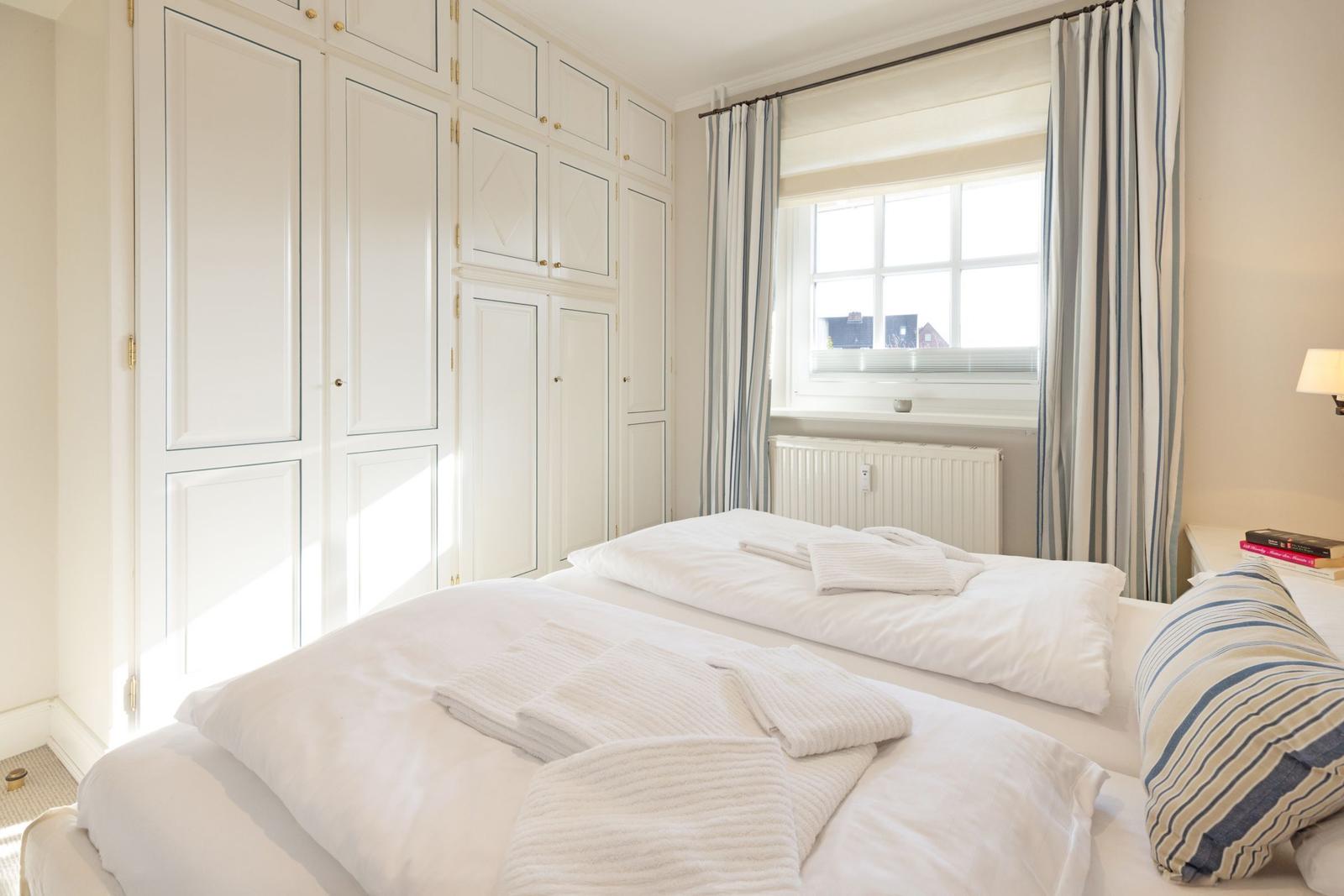 Zimmer mit Doppelbett, weißen Gardinen und großen Schränken.