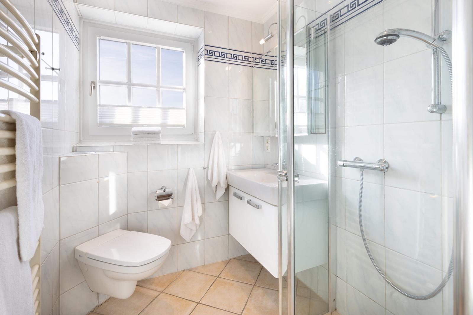 Badezimmer mit Dusche, Waschbecken und Toilette. Fenster mit Blick nach draußen.