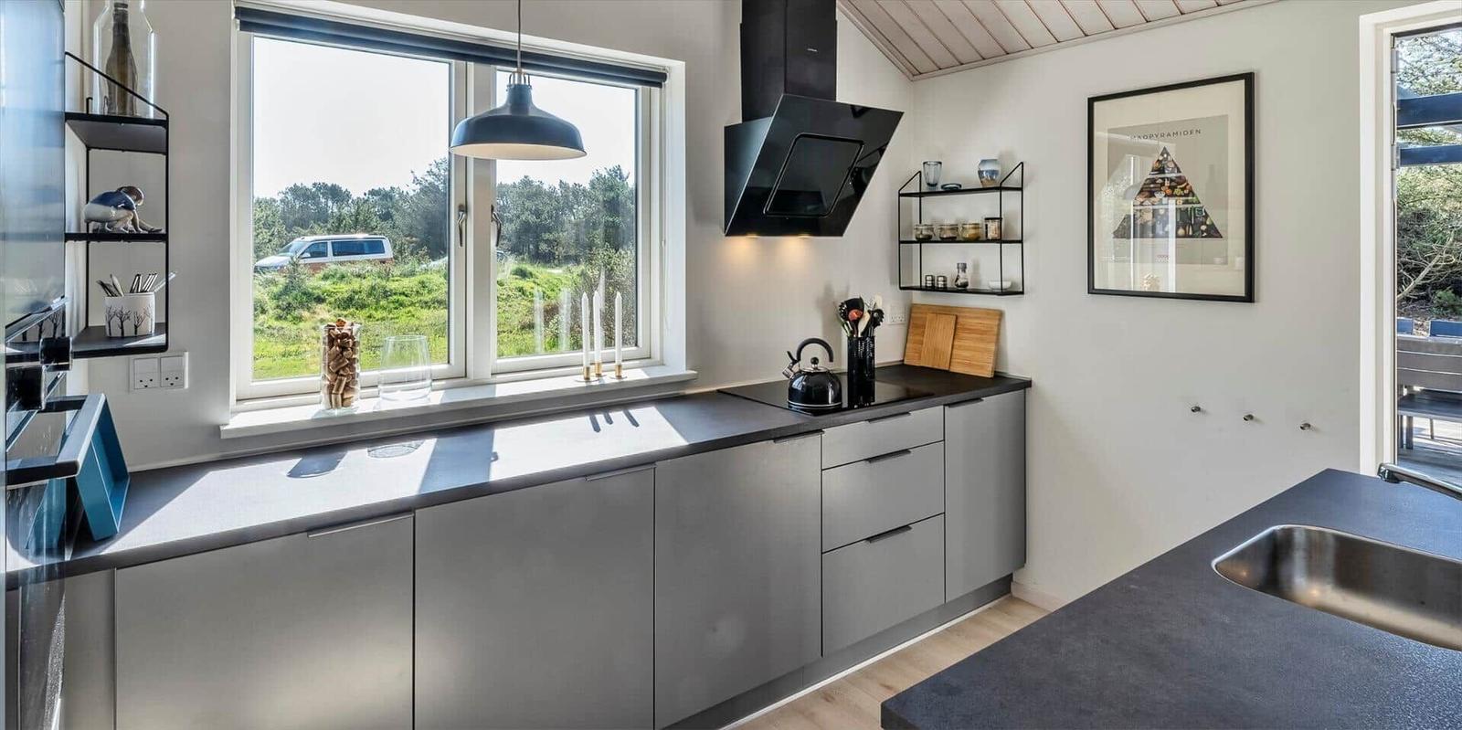 Küche mit grauen Schränken, schwarzer Arbeitsplatte und großem Fenster mit Blick auf Grünland.