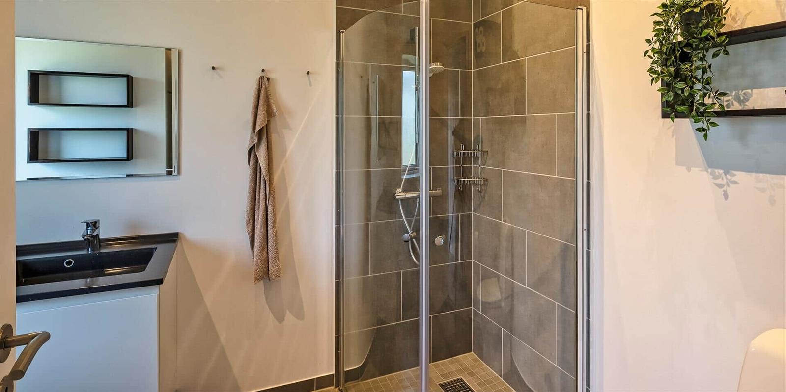 Dusche mit Glaswand, Waschbecken und Spiegel im Badezimmer.