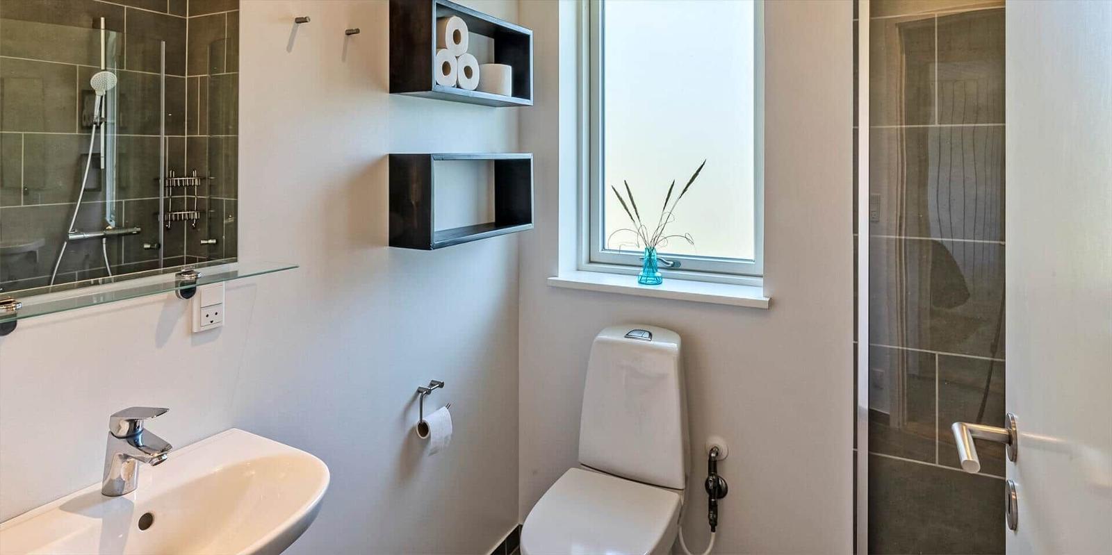 Badezimmer mit Toilette, Waschbecken und Dusche. Fenster mit Blumenvase.