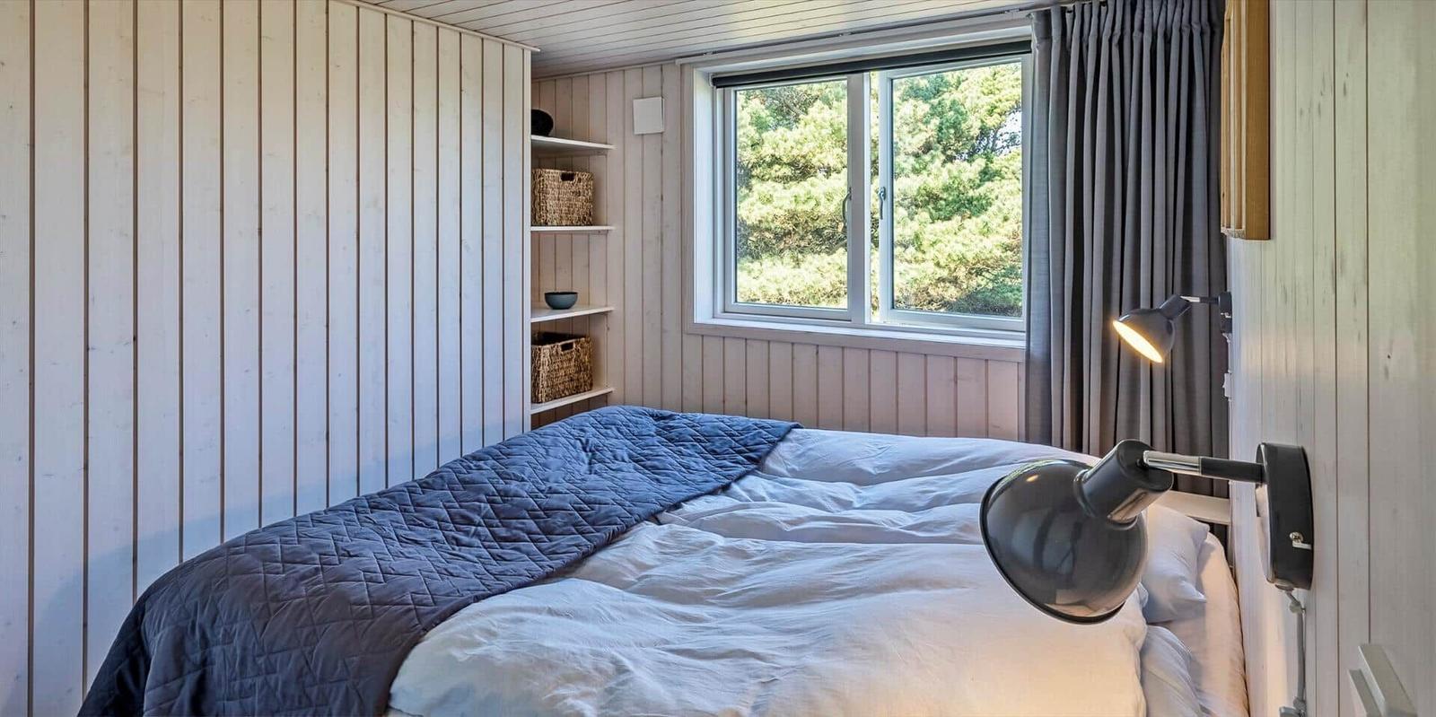 Schlafzimmer mit Bett, Fenster und Wandlampe.