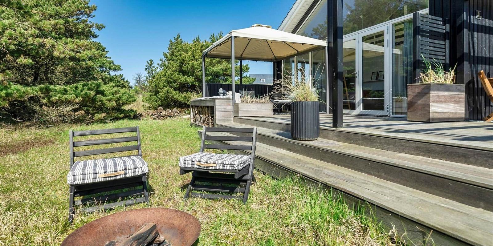 Außenbereich mit Terrasse, Sitzgelegenheiten und Feuerkorb. Moderne Architektur mit Glasfassade.