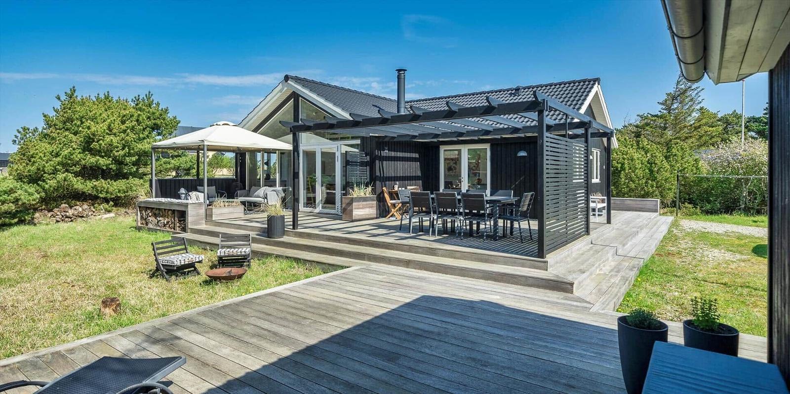 Moderne Villa mit großem Holzdeck, Sitzbereich und Grillplatz im Garten.