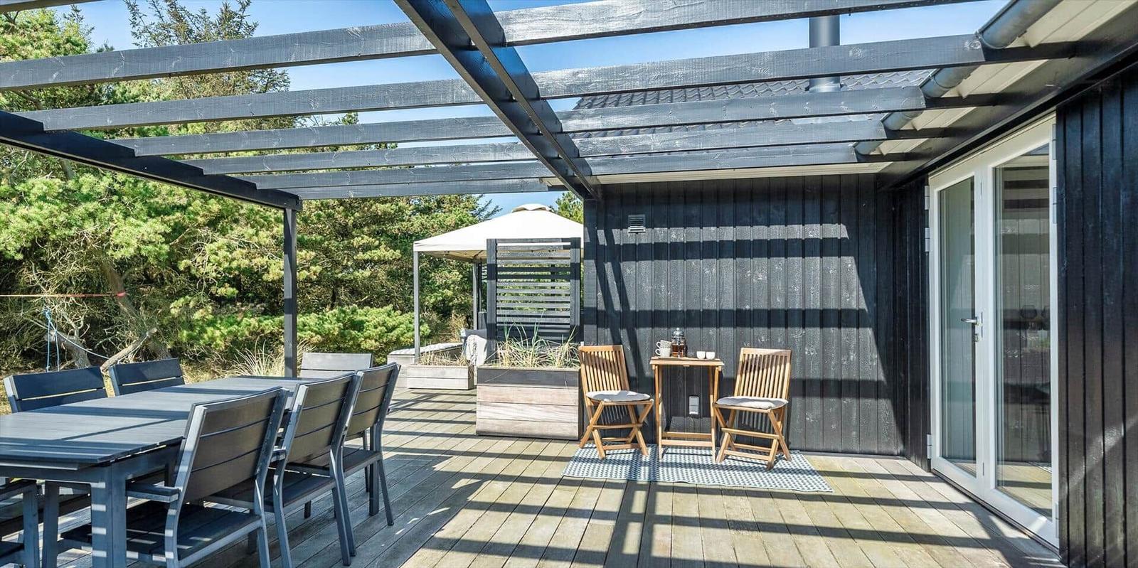 Terrasse mit Tisch, Stühlen und Pavillon. Holzwand und Glastüren sind sichtbar.