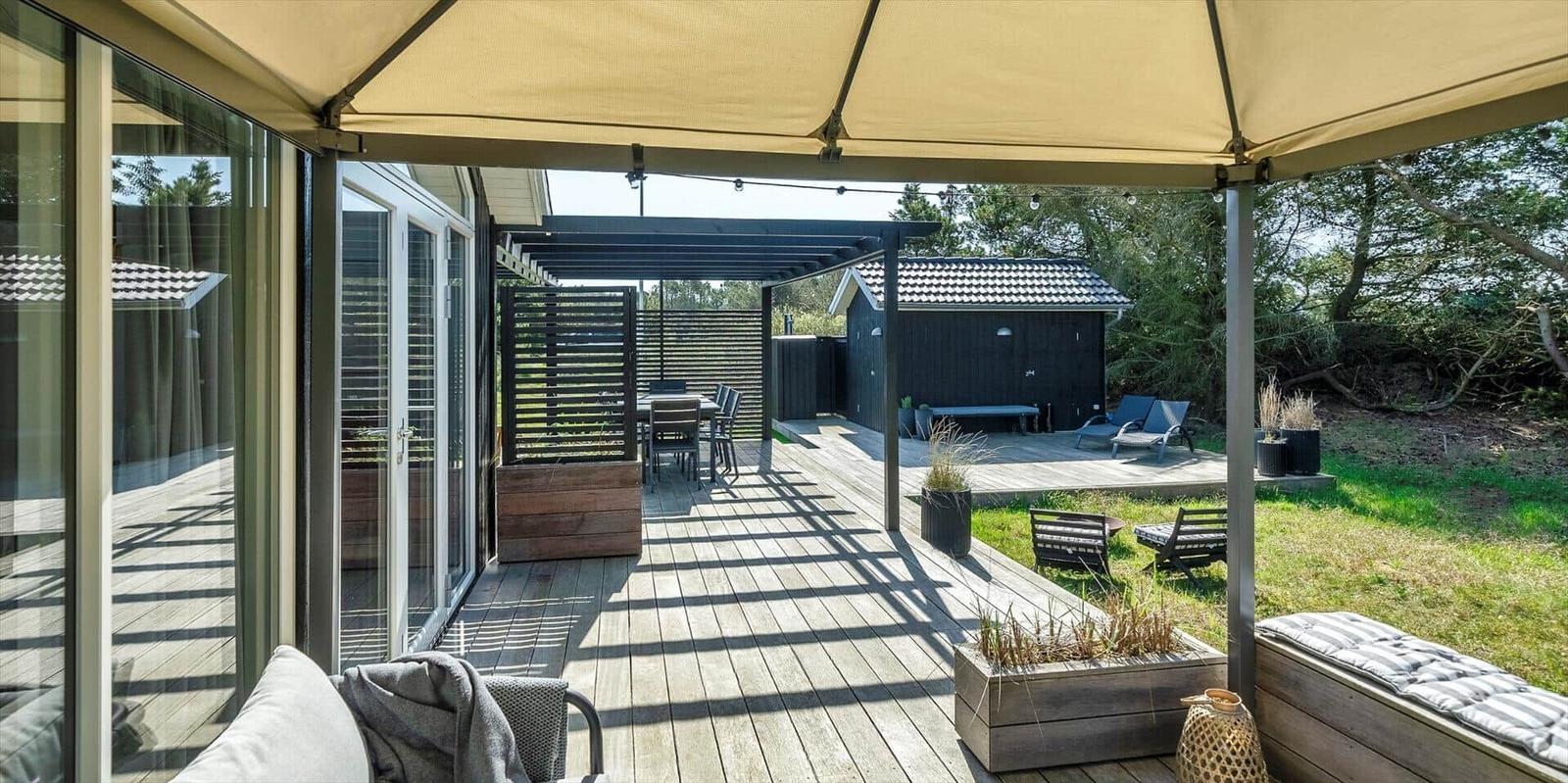 Terrasse mit Sonnensegel, Sitzgelegenheiten und Blick auf Garten und Pavillon.