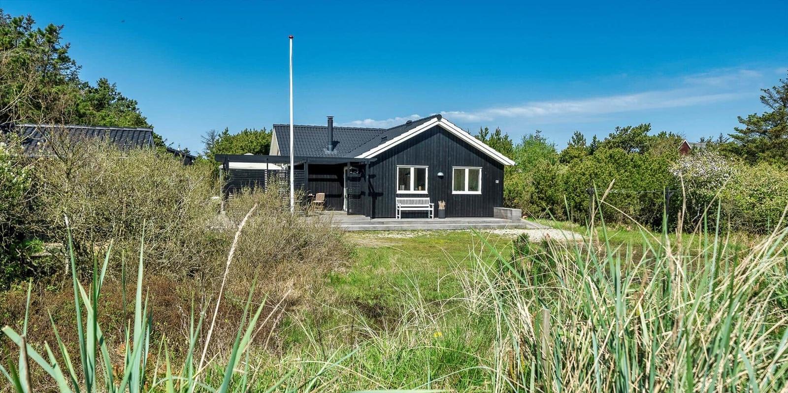 Schwarzes Holzhaus mit Terrasse und weißem Sitzmöbel im Grasland.