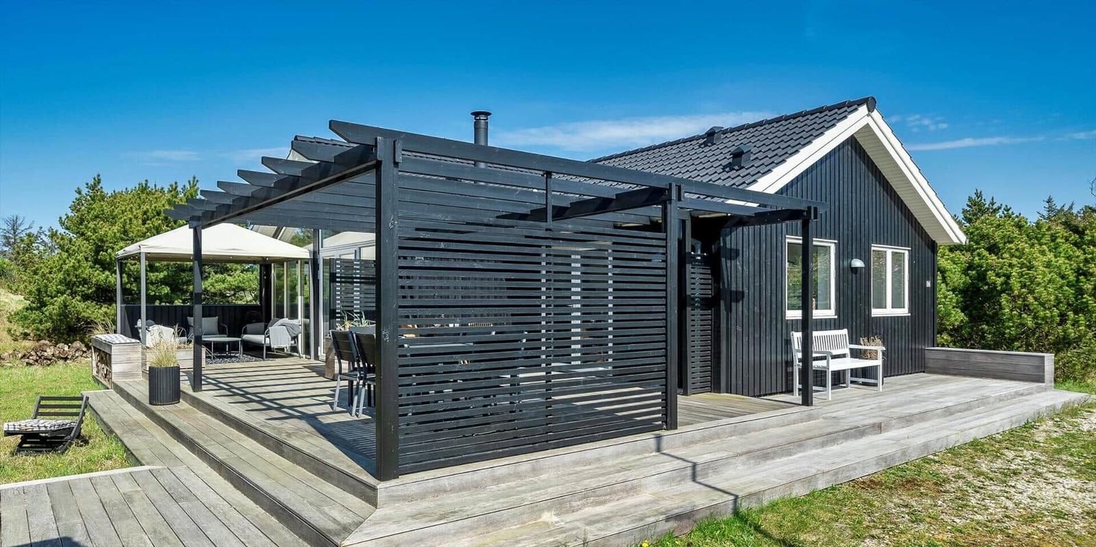 Moderne schwarze Hütte mit Terrasse und Sitzgelegenheiten im Freien.