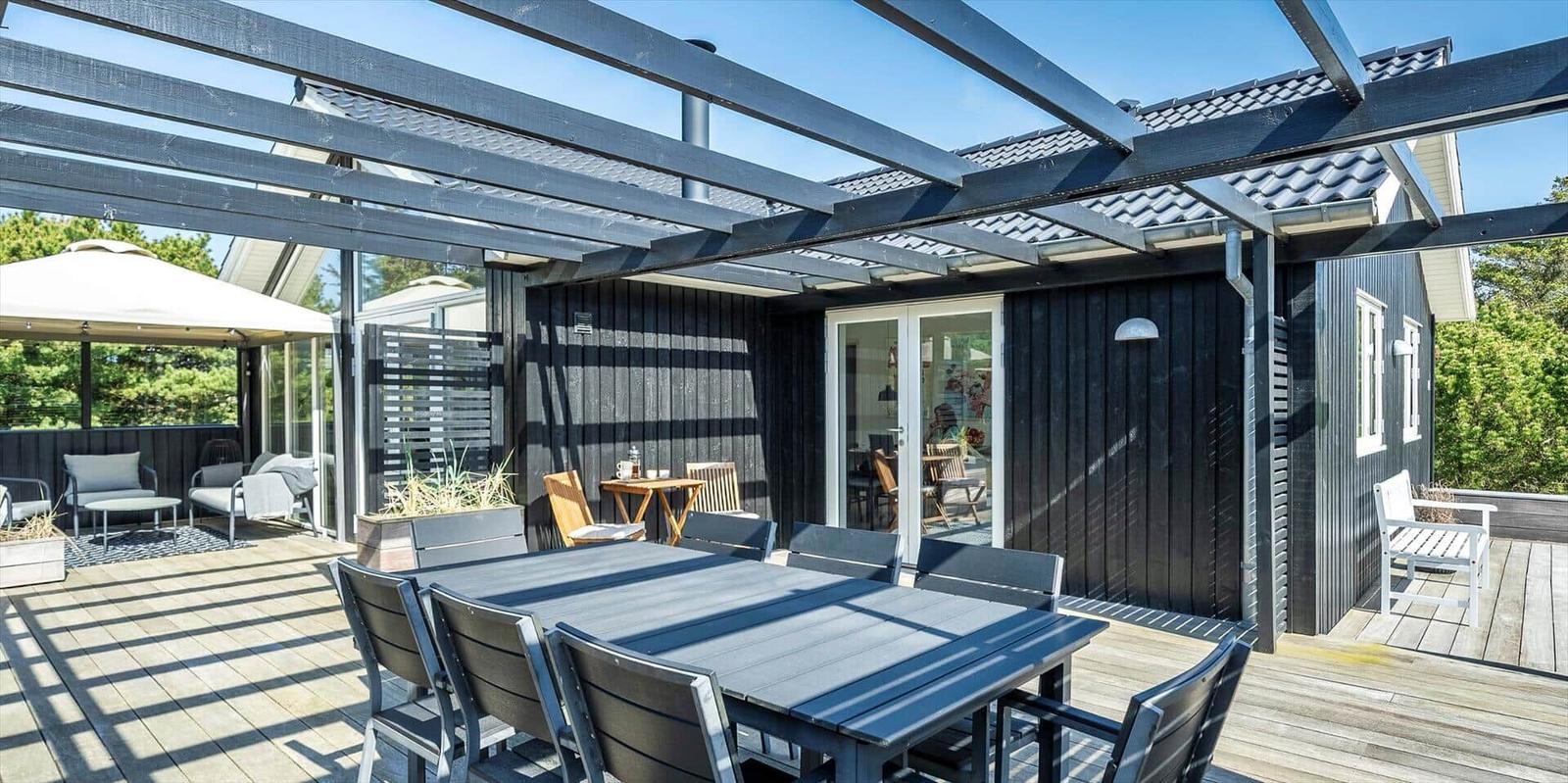 Terrasse mit Tisch, Stühlen und Pavillon. Durchgehendes Glasfenster zum Innenraum.