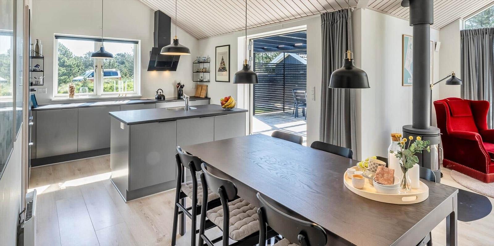 Moderne Küche mit Essbereich und rotem Sessel. Draußen ist eine Terrasse.