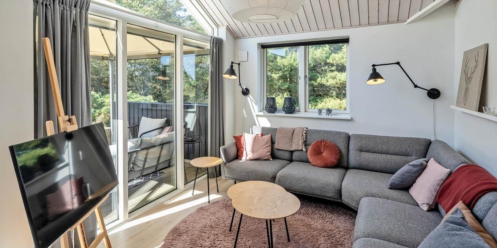 Wohnzimmer mit grauem Sofa, runden Tischen und Blick auf Balkon.