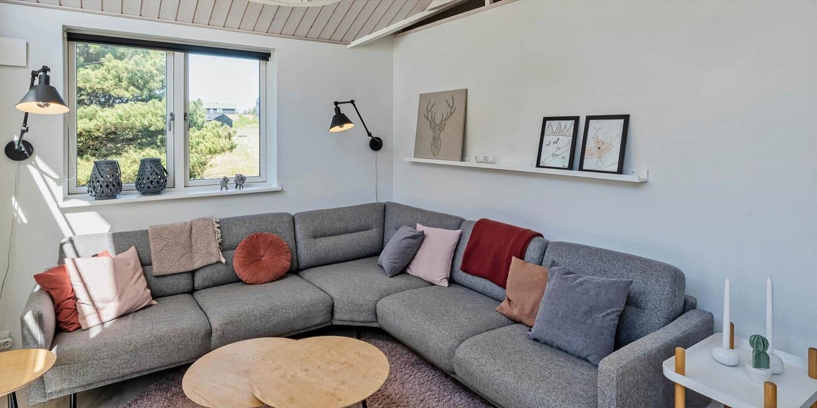 Ein Raum mit grauem Ecksofa, Holztisch und Fensterblick auf Grün.