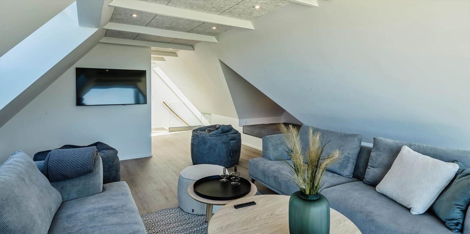 Wohnzimmer mit Sofa, Beistelltisch und Fernseher unter Dachschrägen.
