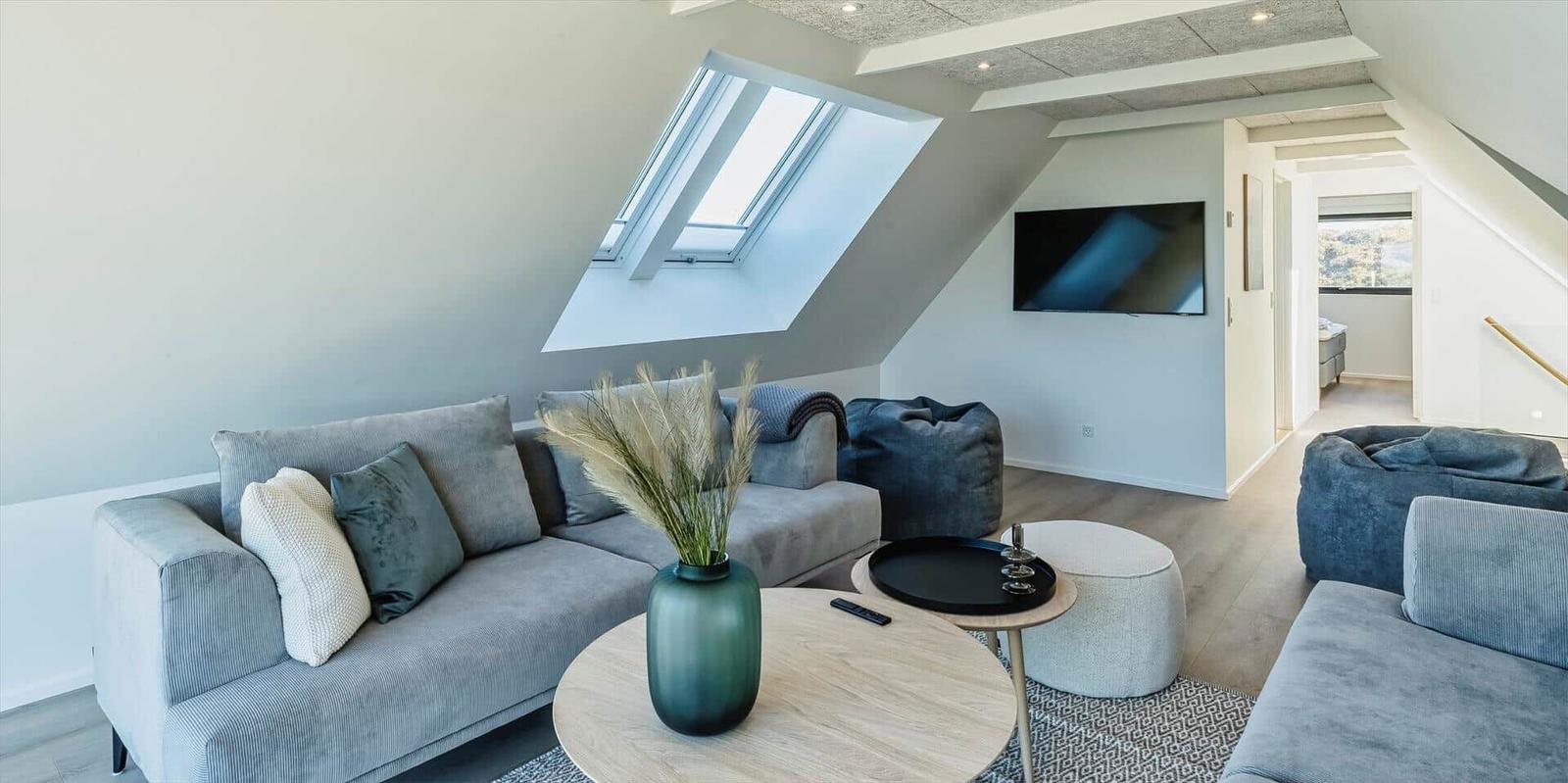 Wohnzimmer mit Sofa, Sitzkissen und TV unter Dachschrägen.