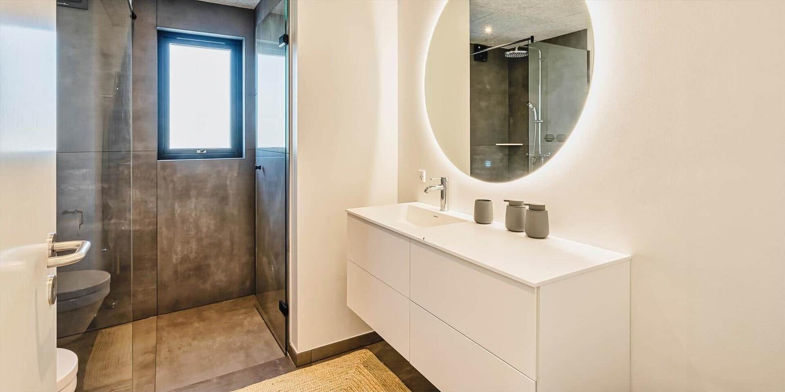 Badezimmer mit Dusche, Waschbecken und runden Spiegel.